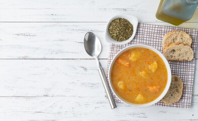 Vegetable soup in a bowl with seasonings and bread slices over wooden table with copy space