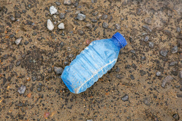 An old dirty plastic bottle lies on the ground. The topic of environmental pollution.