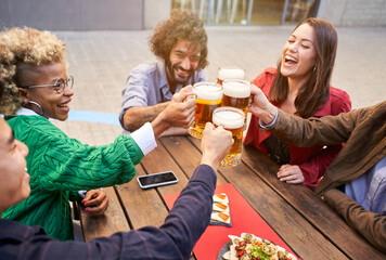 Group of happy friends toasting with beer while having lunch outdoors. The focus is on beers