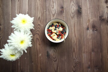 ice cream with berries in bowl and spoon on wooden background and white flowers