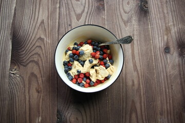 ice cream with berries in bowl and spoon on wooden background