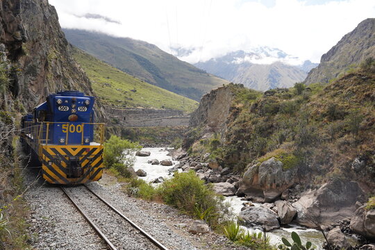Blue train driving through the railways of the Urubamba Sacred muntain valley in peru