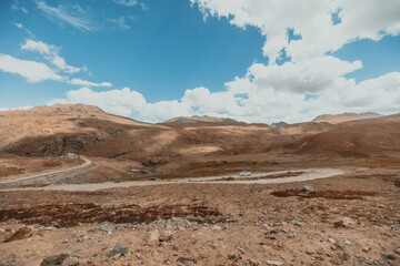 cars driving on a curved mountain road through dry terrain in Deosai National Park in Pakistan