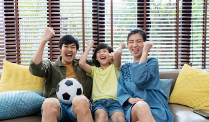 Asian family watching football sports games on TV and reacting happy exiting when team Shoot the...
