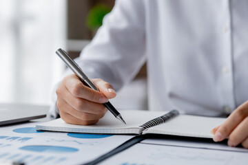 A businesswoman is taking notes in a notebook, she checks company financial documents and she takes corrective reports to the finance manager for correction. Finance concept.