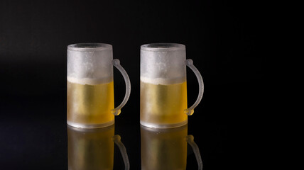 View of two mug of cold beer on a black background