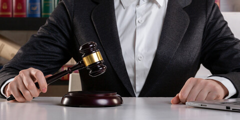 Female judge hands in formal wear with maroon auction gavel and open laptop on a desk surface in an office, front view, selected focus.
