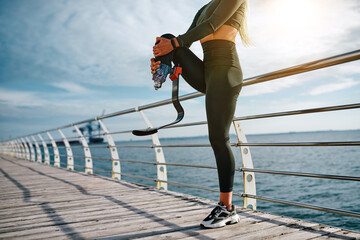 Cropped photo of athletic woman with prosthetic leg stretching at sunrise in the morning. Sport,...