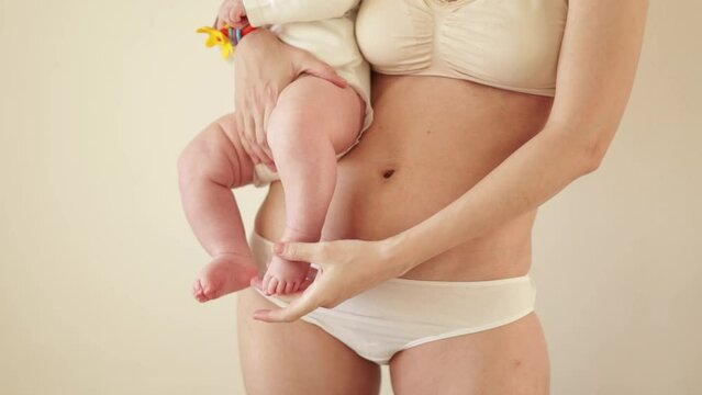 A young mother in underwear with a scar from a cesarean section holds her baby in her arms. Body positivity. real motherhood Natural warm tones. Lifestyle