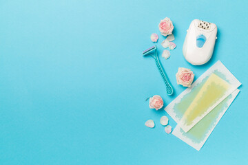 Wax strips, modern epilator and razor with flowers on color background, top view