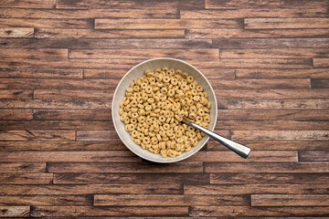 Cereals in a white bowl with a spoon on a wooden table. Round cornflakes for breakfast. Looking down from above. Delicious wheat loops are a snack in the morning. Organic whole grain food.