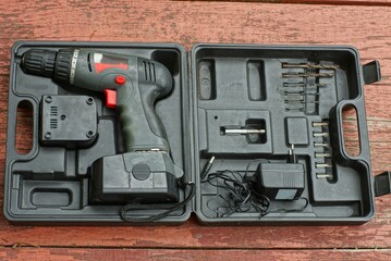 a modern gray plastic screwdriver with a set of iron drills lies and a rechargeable battery lies in...