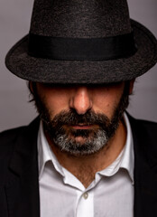 Retrato de hombre joven con barba vestido de chaqueta con un sombrero tapándole los ojos