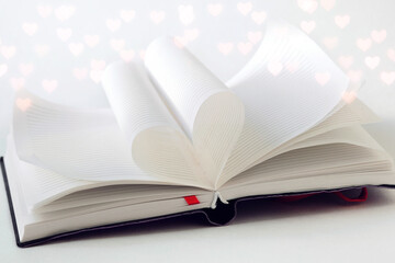 Open book, two pages in the book are folded in the shape of a love heart, bokeh hearts around, love to read books, valentines day background