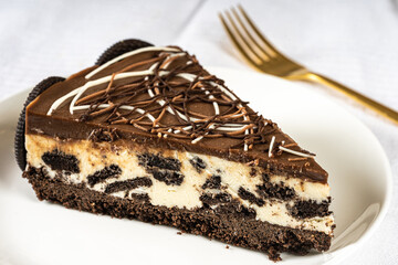 Portion of decorated oreo cheesecake on white table with cutlery and cookies on plate