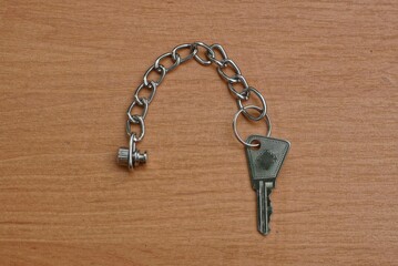Fototapeta na wymiar metal small shiny key from the lock for doors with a chain lies on a beige wooden surface