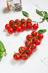 Fresh cherry tomatoes and basil with spices on a white wooden background