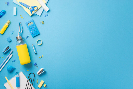 Back to school concept. Top view photo of school supplies yellow drink bottle correction pen clip stapler eraser notepad adhesive tape calculator scissors ruler isolated blue background with copyspace