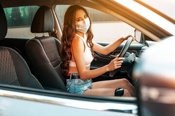 Pretty asian woman in a medical face mask driving car. Quarantine measures during epidemic concept.