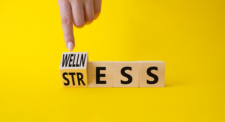 Wellness and Stress symbol. Busnessman hand. Turned Wooden cubes with word Wellness and Stress. Beautiful yellow background. Business and Wellness and Stress concept. Copy space.