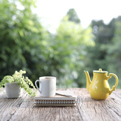White tea cup and yellow vintage tea pot and small plants on wooden table
