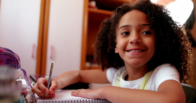 Cute schoolgirl smiling at camera while doing homework