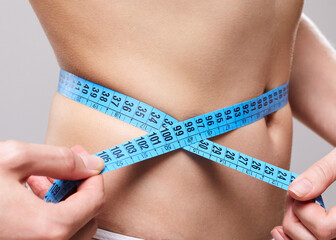 a tanned woman with a blue centimeter measures the waist volume while on a diet