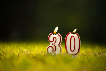 Candles in the form of the number 30 on a green summer background. Thirtieth anniversary. Congratulations on the anniversary of thirty years. - obrazy, fototapety, plakaty