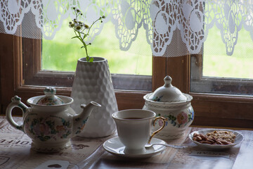 a tea set and a vase with daisies on the table in front of a wooden window of a rural house