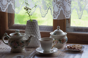 Fototapeta na wymiar a tea set and a vase with daisies on the table in front of a wooden window of a rural house