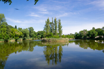 Fototapeta na wymiar City park with a pond and a fountain. Zorbig, Germany. A small island in the middle of the pond.