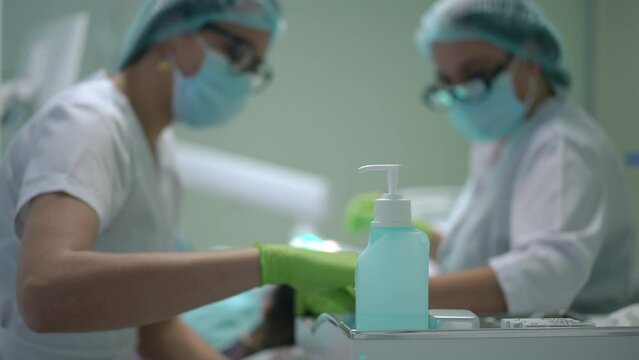 Disinfectant in dental office with blurred doctor and assistant curing patient at background. Caucasian professional women in face mask treating client in medical clinic. Insurance and medicine
