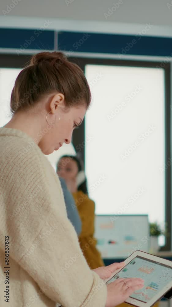 Poster woman holding digital tablet zooming in on sales pie chart and comparing data with statistics on lap
