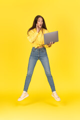 Shocked Female Holding Laptop Jumping Over Yellow Background, Vertical