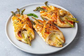 Baked green asparagus with ham and cheese in puff pastry sprinkled with sesame seeds and green basil leaves.