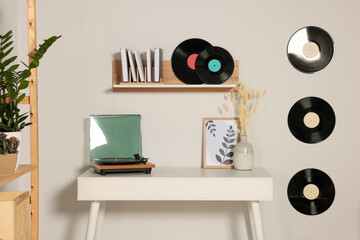 Table and stylish turntable near white wall decorated with vinyl records - obrazy, fototapety, plakaty
