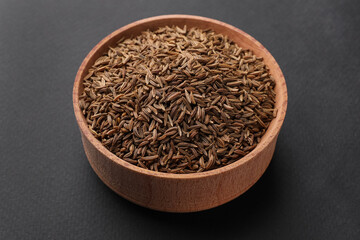 Wooden bowl with cumin seeds on grey background