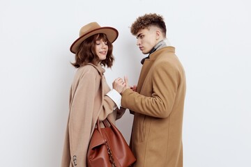 a happy couple in love is standing in beige stylish autumn coats on a white background and a man is holding a woman's hands smiling pleasantly