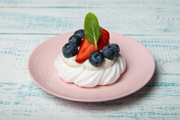 Pavlova cake with strawberries and blueberries and mint on a pink platter. Home confectionery. Old retro white and blue table.
