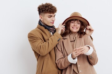 a sweet, loving couple stands on a white background in autumn clothes and the guy adjusts the hat on the head of a joyful woman looking at her with snow. Horizontal photo