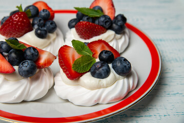 Four cakes Anna Pavlova with blueberries and strawberries with a mint leaf on a beautiful plate. Home confectionery. Old retro white and blue table.