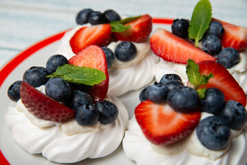 Four cakes Anna Pavlova with blueberries and strawberries with a mint leaf on a beautiful plate. Home confectionery. Old retro white and blue table.
