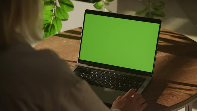 Handheld shot of a woman watching laptop computer with green screen chroma key indoors
