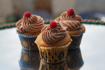 Beige cupcakes made of delicate light sponge cake decorated with chocolate cream. Topped with ripe raspberries.
