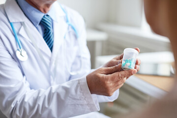 Close-up of unrecognizable male doctor in lab coat holding pill bottle while recommending drugs to patient at appointment - obrazy, fototapety, plakaty