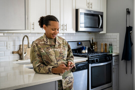 U.S. Army female soldier on her phone in her kitchen