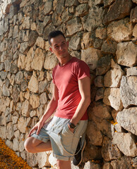 A young man in a red T-shirt posing next to a wall.