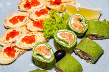 Some green sushi with red fish and pancakes with red caviar close-up