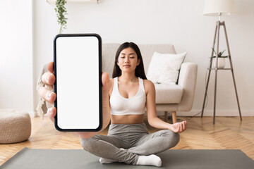 Yoga App. Calm young asian woman meditating and holding big blank smartphone