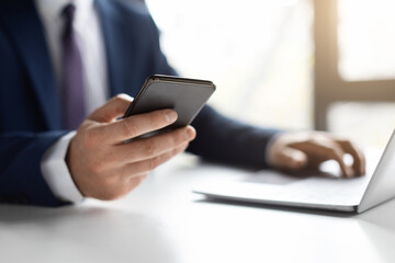 Unrecognizable Male Entrepreneur Using Smartphone And Working With Laptop In Office